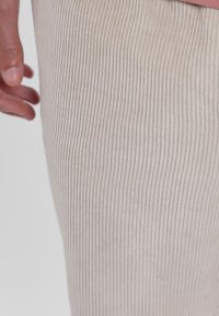 Tissu côtelé beige clair en gros plan, présentant des lignes verticales et une texture douce, avec une partie de main visible sur le bord.