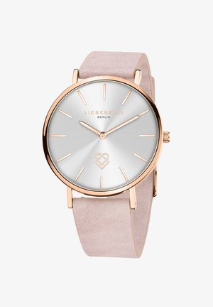 Rosenfarvet ur med en sølvfarvet solstråledial, tynde time- og minutvisere samt et lys rosa suede rem. Har minimalistiske markører og branding.