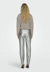 Zilveren metallic broek met een hoge taille, twee achterzakken, gecombineerd met een zacht beige trui. Glad textuur, rechte pijpen.