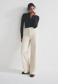 Beige high-waisted wide-leg jeans with a button closure, paired with a fitted black long-sleeve polo shirt. Smooth texture, casual style.