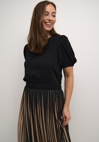 Juodas viršus su pūstomis rankovėmis, derinamas su raukšlėta sijona, kuris turi pakaitomis juodas ir kremines raudonas juostas, sklandų tekstūrą ir elastingą juosmenį.