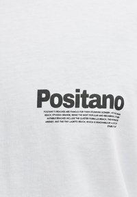 Tissu blanc avec texte noir "Positano" et une brève description des plages de Positano imprimée en dessous en police plus petite.