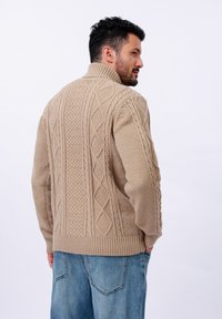 Pull en tricot beige avec des motifs texturés, doté d'un col montant et d'un ourlet côtelé, associé à un jean en denim bleu clair.