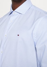 Himmelblaues kariertes Hemd aus einem Stoff mit glatter Textur. Verfügt über einen Button-Down-Kragen und ein kleines gesticktes Logo auf der Brust.