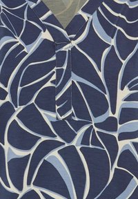 Marineblauwe stof met witte abstracte bladerenpatronen. Heeft een V-hals met een sleutelgatdetail in het midden. Glad textuur.