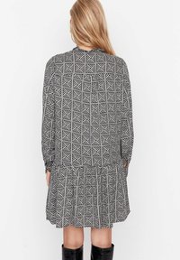 Schwarz-weißes geometrisches Musterkleid mit langen Ärmeln, plissiertem Rock und Rundhalsausschnitt, das mit einem gerafften Detail am Rücken versehen ist.