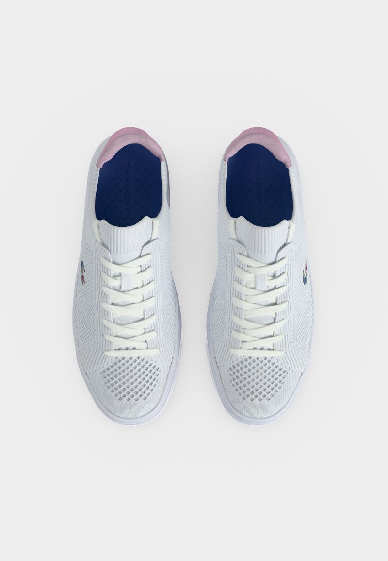 Paar weiße Strick-Sneaker mit weißen Schnürsenkeln, pinkfarbenen Fersenakzenten und blauen Innensohlen auf hellem, einfarbigem Hintergrund.