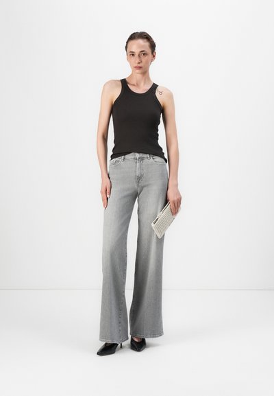 Jeans grii evazați asortați cu un top negru mlădios. Ținuta include o geantă țesută albă și pantofi negri cu bot ascuțit.