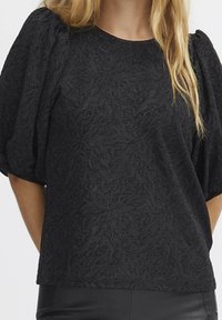 Top nero in tessuto texturizzato con maniche a sbuffo e motivo floreale, realizzato in tessuto leggero e con scollatura rotonda.