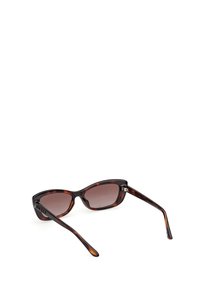 Occhiali da sole tortoiseshell marroni con forma a occhio di gatto, lenti marroni sfumate e braccia slanciate e affusolate. Presentano un branding minimalista sulla tempia.