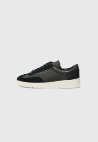 Low-top sneakers featuring a mix of black suede and textured leather, a white rubber sole, and black laces. Subtle branding on the side.