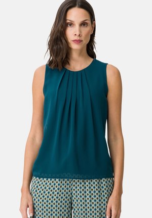 Teal sleeveless blouse with pleats at the neckline and a scalloped hem. The fabric has a smooth texture, shown with patterned pants.