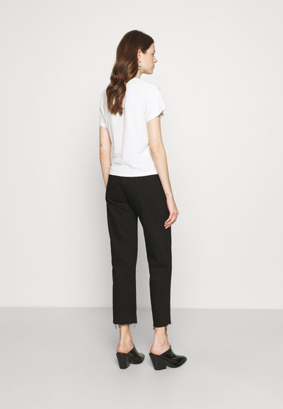 Black cropped jeans with frayed hem, paired with a fitted white t-shirt. Model wearing black heeled mules. Simple, minimal design.