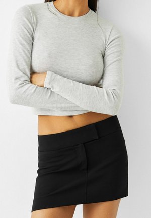 Crop top gris clair à manches longues associé à une mini jupe noire ajustée avec une large taille et une texture lisse.
