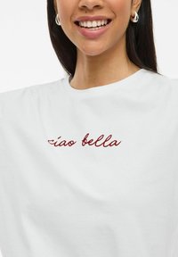 T-shirt en coton blanc à coupe décontractée. Présente un texte en rouge "ciao bella" sur le devant. Texture lisse, col rond classique.