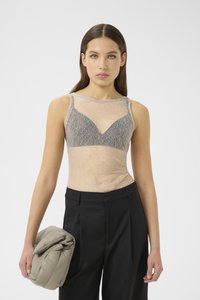 Top beige trasparente con motivo in pizzo e accenti grigi, con un design aderente e spalline larghe, abbinato a pantaloni neri a vita alta e una borsa grigia.