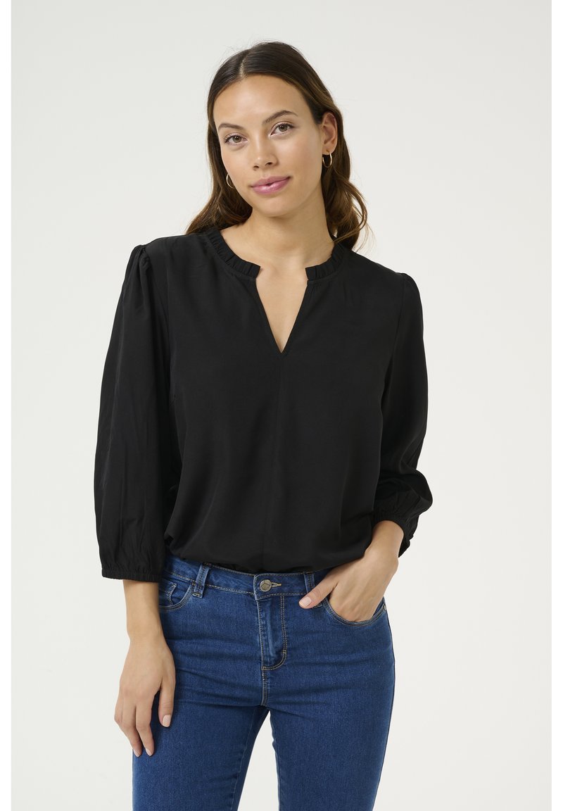 Black blouse with a V-neck and ruffled collar, long puff sleeves, made from a smooth fabric, paired with blue jeans.