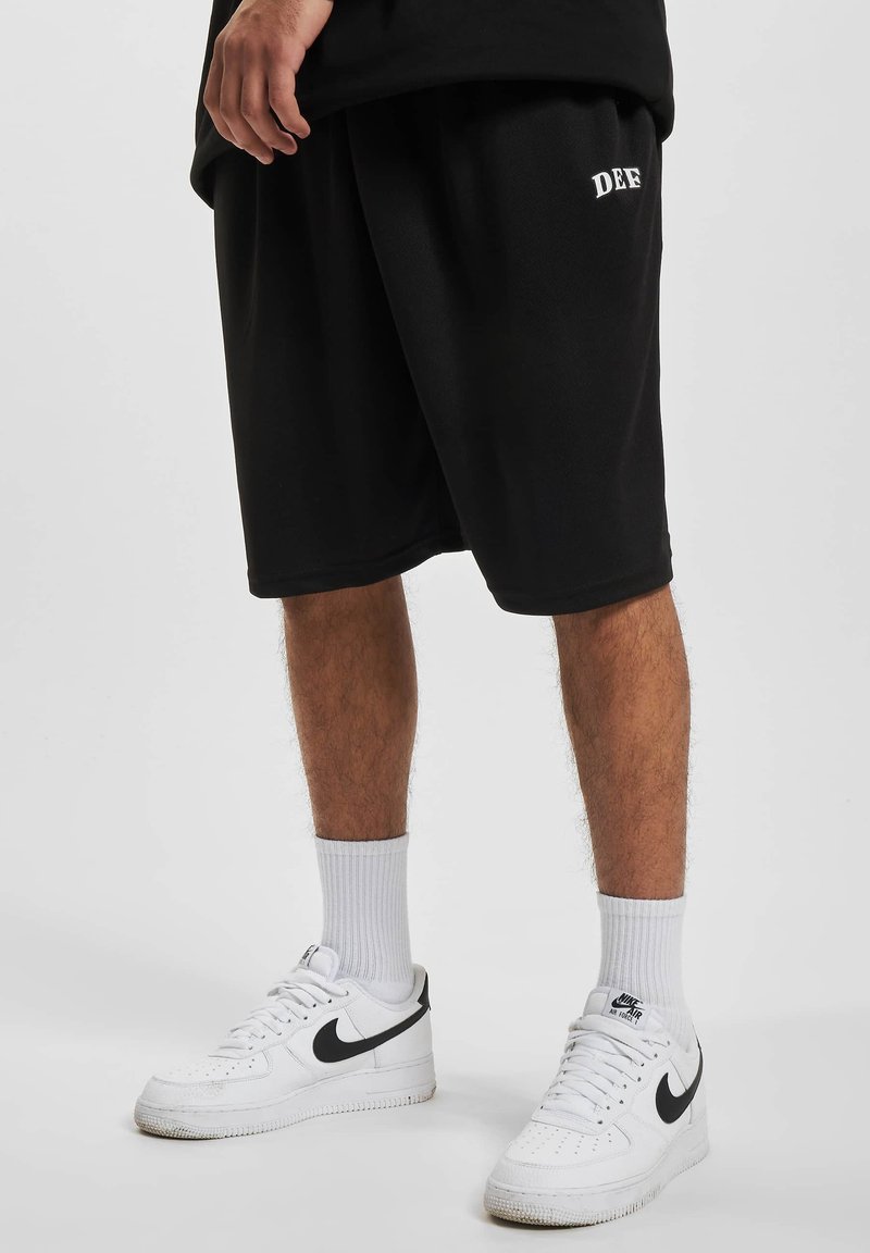Sorte sportshorts lavet af et struktureret stof, med et hvidt logo. Kombineret med hvide sneakers og ribbede hvide strømper.