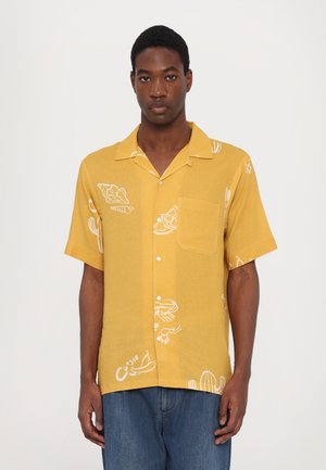 Korte mouwen, geknoopt shirt in mosterdgeel met witte grafische patronen, waaronder cactussen, citrusvruchten en zeevruchten. Detail van een voorzak.