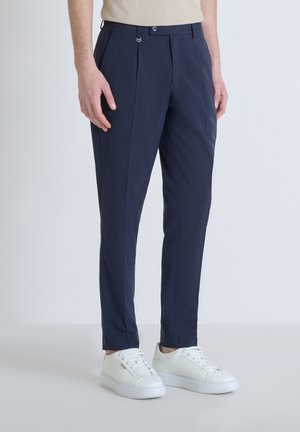 Marineblauwe broek met plooien, gemaakt van lichtgewicht stof, met riemlussen en een knoopsluiting, gecombineerd met witte sneakers.