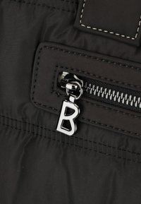 Tessuto in nylon nero con una tasca con zip e un tirante in metallo argento con un ciondolo a forma di "B". La cucitura è di un bianco a contrasto.