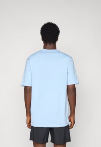 Šviesiai mėlynas medvilninis marškinėliai su trumpomis rankovėmis, laisvas siluetas, apvalus iškirpimas ir lygus paviršius, dėvimi virš juodų šortų.