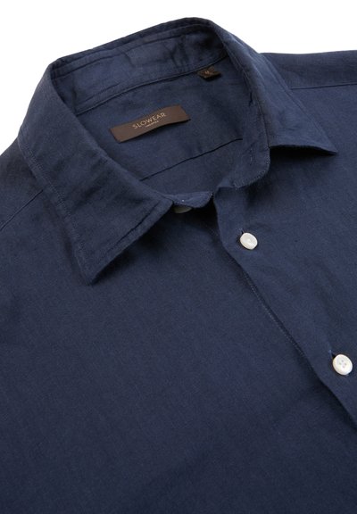 Camisa azul marino abotonada con cuello puntiagudo y dos botones blancos visibles, mostrando la etiqueta de la marca Slowear en el interior del cuello.