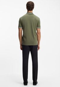 Ciemnozielona koszulka polo z krótkim rękawem, z białymi i czarnymi paskami na kołnierzyku i rękawach, zestawiona z czarnymi spodniami i butami.