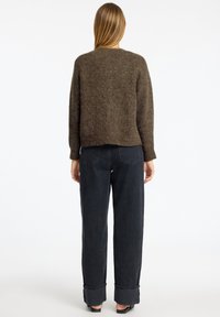Brauner Strickpullover mit lässigem Schnitt und geripptem Saum, kombiniert mit hoch taillierten, dunklen Denim-Hosen mit umgeschlagenen Bündchen.