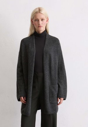 Grijze cardigan van zacht materiaal, met een open voorkant, lange mouwen, zakken en een ontspannen pasvorm. Draag over een zwarte coltrui.