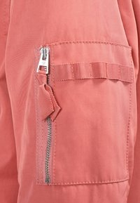 Cargo kalhoty z jemné korálové látky, s vertikální kapsou na zip a texturovaným detailem pásku, s hladkým, matným povrchem.