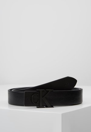 Ceinture en cuir noir avec boucle en métal noir embossée des initiales "CK" et de l'inscription "Calvin Klein Jeans", présentée enroulée sur une surface blanche.