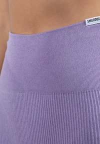Détail de la taille côtelée violette avec une texture lisse. Présente une petite étiquette avec un texte noir. Conçu pour un ajustement près du corps, tissu doux.