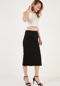 Fehér bordás cropped top keresztbe fűzött pántokkal, fekete midi ceruzaszoknyával párosítva. A modellen fekete magassarkú szandál és nagy fekete fülbevaló található.