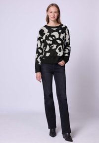 Maglione lavorato a maglia con motivo astratto in bianco e nero, scollo rotondo, polsini e orlo a coste, abbinato a jeans scuri e stivali alla caviglia neri.