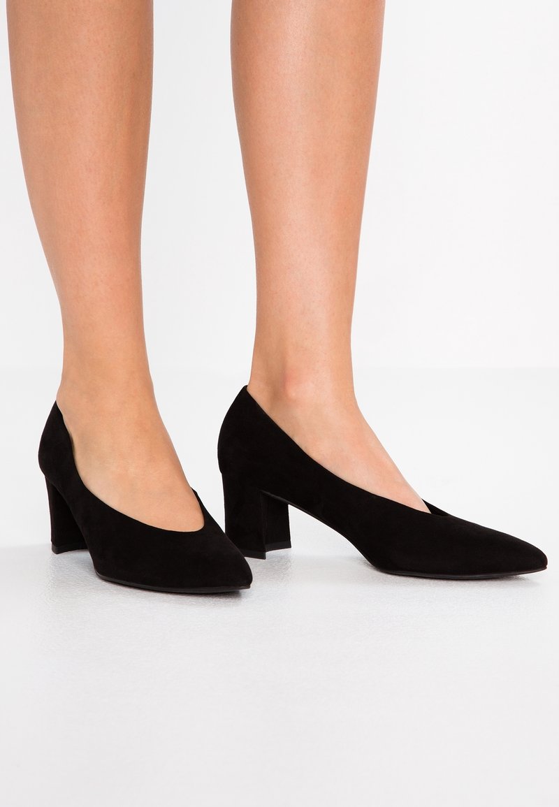 Escarpins à talons blocs en daim noir avec un bout pointu et un design supérieur découpé en forme de V, présentant une texture lisse et une couleur unie.