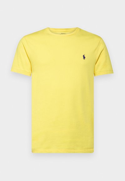 Κίτρινη βαμβακερή μπλούζα με κοντά μανίκια, στρογγυλή λαιμόκοψη και πορφυρό κεντημένο λογότυπο στο αριστερό στήθος. Λεια υφή, casual εφαρμογή.