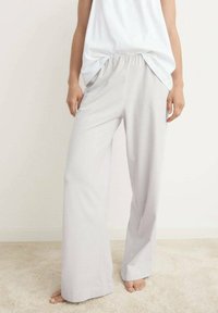 Lichtgrijze wijde broek van zacht materiaal, met een elastische tailleband en een gladde textuur, gecombineerd met een witte top.