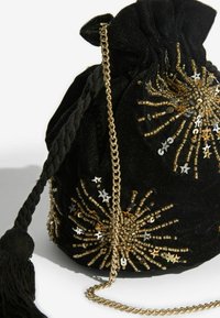 Čierna zamatová taštička so sťahovacou šnúrkou, zdobená zlatými a striebornými korálkami usporiadanými do vzoru hviezdneho výbuchu, so zlatým reťazovým remienkom a detailom s strapcom.