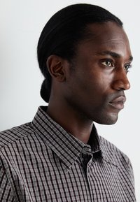 Checked shirt in dark colors with a collar, featuring a button placket and subtle detailing. Smooth fabric with a tailored fit.