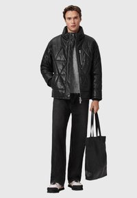 Polstret sort læderjakke med diamantmønster, lynlås lukning, grå sweater under, sorte vidde jeans og en struktureret sort tote bag.