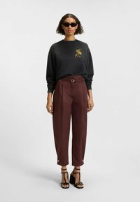 Svart sweatshirt med en blommig grafik, parat med burgunderfärgade högmidjade byxor med ett bälte och knappramar. Svarta remsandaler.