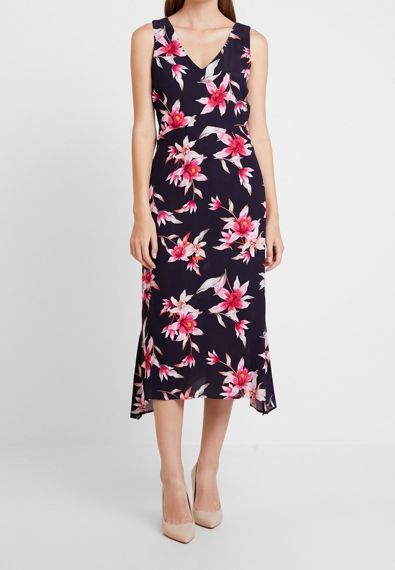 Robe midi florale avec une base marine, ornée de fleurs roses et blanches. Décolleté en V, design sans manches et ourlet fluide.