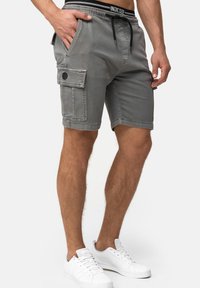 Shorts cargo gris avec taille à cordon, quatre poches et détail de bouton noir ; associés à des baskets blanches. Matériau en mélange de coton.