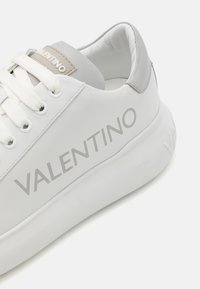 Witte leren sneaker met grijze accenten, voorzien van een gewatteerde kraag, platte veters en het "VALENTINO"-logo in het grijs aan de zijkant.