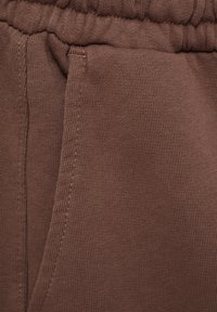 Gros plan sur un tissu marron avec une ceinture élastique et des coutures de poche latérale sur un vêtement.