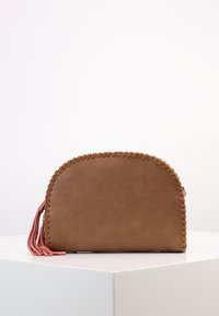 Hnědá kožená taška zaobleného tvaru, se šitými okraji a růžovými třásněmi. Hladký povrch s minimalistickým designem.