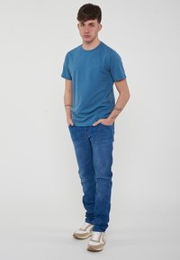 T-shirt blu a girocollo, tessuto morbido, abbinata a jeans azzurri chiari. Le calzature presentano accenti beige e bianchi, con laccetti.