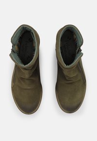Botas de ante verdes hasta el tobillo con un cuello doblado, cremallera lateral y forro de tela a rayas. Suelas planas con detalles de costura.