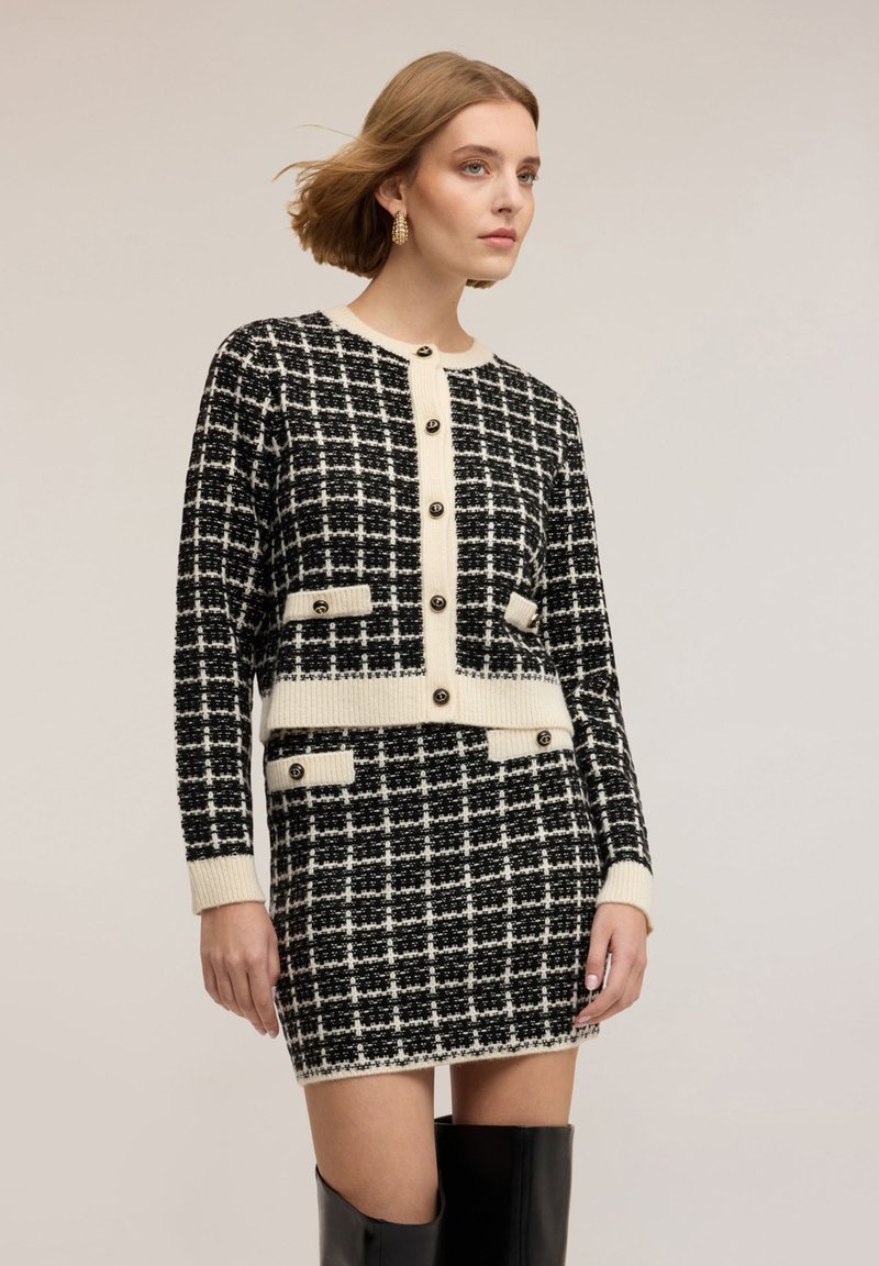 Černobílé šaty s kostkovaným vzorem pepito a k nim ladící krátký kardigan. Má knoflíky, kapsy a žebrované manžety. Elegantní textura látky.